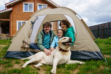 backyard camping. family with a dog are sitting with a tourist tent in the backyard