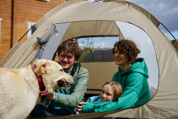 backyard camping. family with a dog are sitting with a tourist tent in the backyard