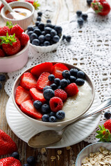 Breakfast bowl, porridge with the addition of fresh berries; strawberries, blueberries and raspberries in a ceramic bowl on a rustic table.