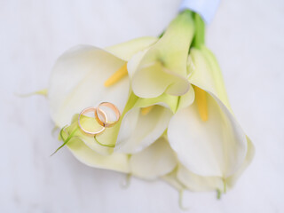 Wedding rings on a background of a beautiful wedding bouquet of white calla lilies on a white table. High quality photo