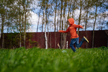 A boy in an orange hoodie is playing soccer and kicking a ball in the backyard