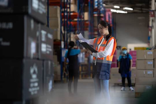Professional beautiful asian woman worker checks stock and inventory with holding clipboard in the retail warehouse full of shelves with goods. Working in logistics, Distribution center. - Powered by Adobe