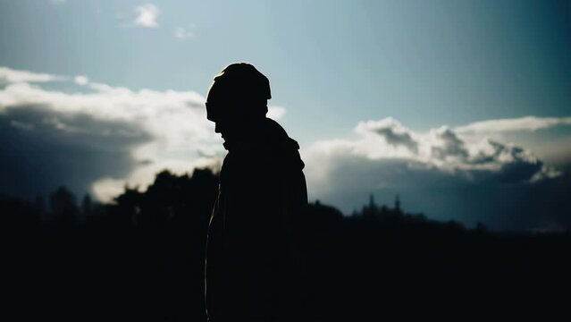 The silhouette of a teenager walking against the background of clouds and sky. a boy walks outside the city
