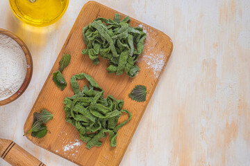 Cooking homemade nettle noodles, prepared sliced tagliatelle on a wooden board on a light concrete background. Recipes with wild herbs.