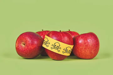 Apples with poison skull symbol sticker on green background. Concept of pesticide residues in...