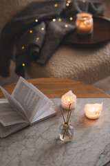 Fototapeta na wymiar Liquid home fragrance in diffuser with open paper book on coffee table in bedroom indoors close up over scented candle. Cozy and hygge atmosphere. Aromatherapy.