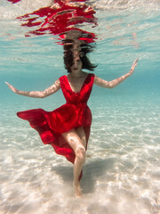 Mystical underwater portrait of beautiful asian young woman in red dress. Girl swimming underwater,...