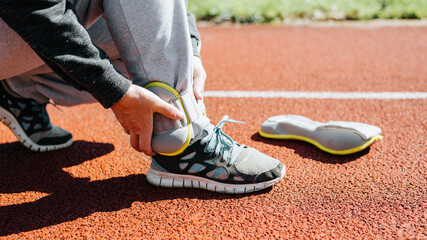 Woman using fitness leg weights while exercising on treadmill in stadium, outdoors. Sports equipment for training and weight loss. Close-up, side view