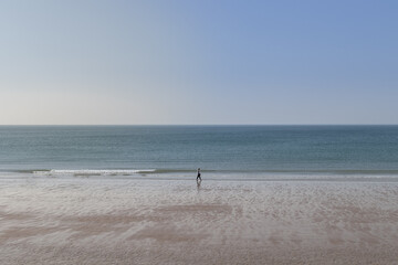 Fototapeta premium Promeneur sur la grande plage de St-Hélier sur l'île anglo normande de Jersey. La mer est calme et le ciel d'un grand bleu