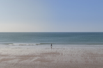 Fototapeta na wymiar Promeneur sur la grande plage de St-Hélier sur l'île anglo normande de Jersey. La mer est calme et le ciel d'un grand bleu
