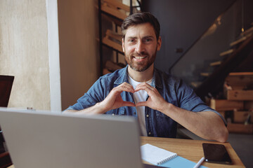 Handsome happy man showing heart gesture and smiling in cafe. Love expression concept. Portrait shot