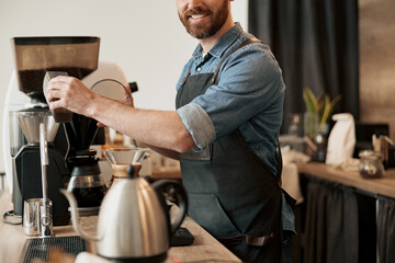 Close up of Barista pours coffee beans into coffee machine tank for grinding standing behind counter