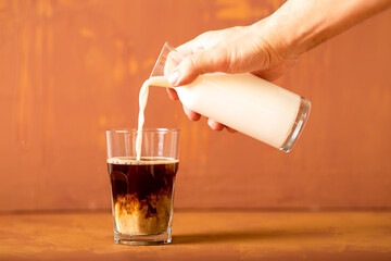 Hand is pouring milk to brewed coffee in studio with copy space.