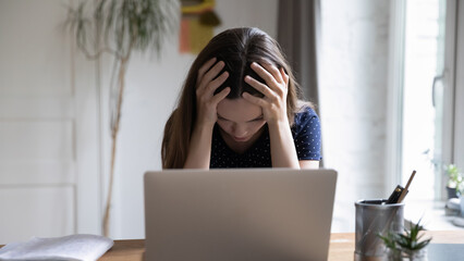 Frustrated unhappy laptop user girl touching head at work table with computer, going through...