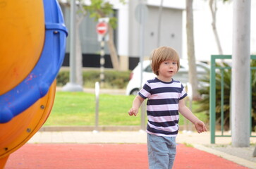 A blond boy in a striped T-shirt walks on the street.