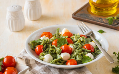 Homemade nettle tagliatelle with poached cherry tomatoes and mozzarella in a gray plate on a light concrete background. Italian food.