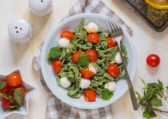 Homemade nettle tagliatelle with poached cherry tomatoes and mozzarella in a gray plate on a light concrete background. Italian food.