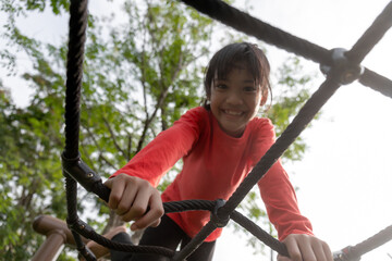 summer, childhood, leisure and people concept - happy little girl on children playground climbing...