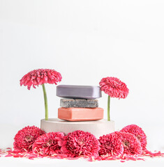 Handmade soap setting with soap bars on podium with pink flowers at white background. Front view.