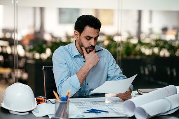 Busy attractive middle eastern arab guy engineer with beard works with documents in office...