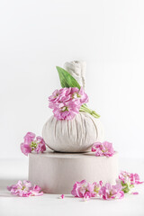 Herbal massage stamp on product podium with pink flowers at white background. Spa setting with wellness tools. Front view.