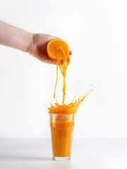 Women hand squeezing orange with splashing juice in glass at white background. Orange juice...