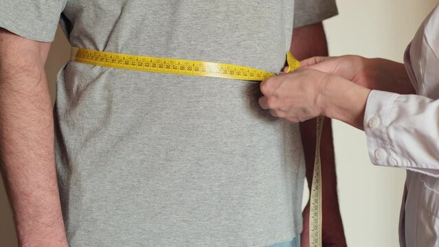 Doctor measuring waist of overweight man during annual medical checkup. Measurement of abdominal volume in a patient with diabetes.