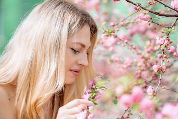 Naklejka premium Blonde woman in white clothes next to a flowering tree or bush with pink flowers