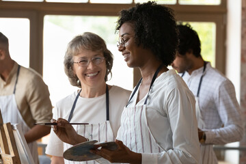 Aged art school teacher and African student laughs at art-class in workshop. Take part in beginner drawing lesson. Gain professional artist education, creative hobby, share experience, tuition concept