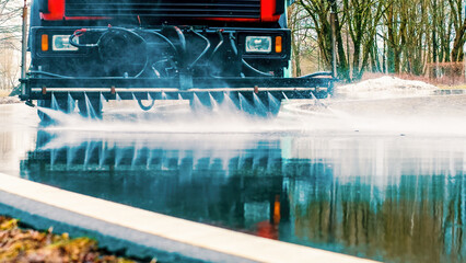 Cleaning sweeper machine washes the asphalt road with water spray