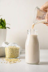 Woman pouring Green Buckwheat milk in bottle. Close up. Dairy free plant based milk replacer. Vertical orientation.