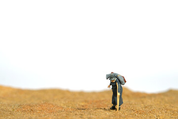 Miniature people toy figure photography. An old men grandfathers walking alone in the desert, moving to refugee camp because of war conflict.
