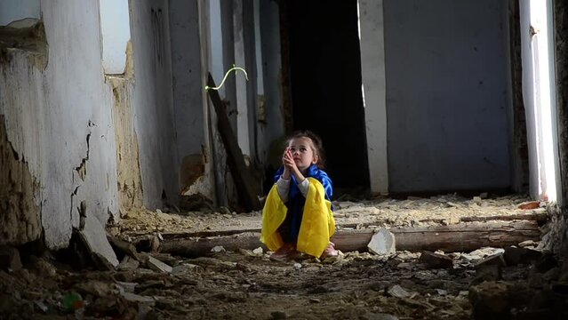 A child prays in a bomb shelter. A child in a war-torn house. War in Ukraine. Consequences of the bombing of Ukrainian cities. Destruction in Ukraine. Ukrainian children against the war.