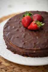 Delicious cake in chocolate glaze with strawberries on a white dish. Puff cake with cream and nuts, decorated with strawberries.