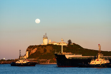 Nobbys head lighthouse across Newcastle Harbour with ship and tugboats, Newcastle, NSW, Australia