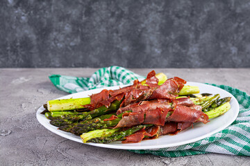 Baked asparagus with bacon and herbs on wooden background
