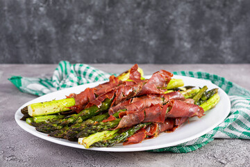 Baked asparagus with bacon and herbs on wooden background