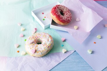 Freshly baked donuts glazed with various pink shades and sprinkled with caramel hearts, lilac shade wrapping paper on the table, Donut Day 