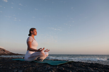 Fototapeta na wymiar Young woman meditation in a yoga pose at the beach on sunset.