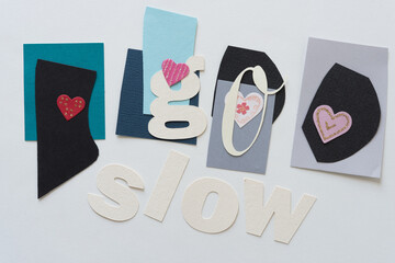 the expression "go slow" in paper letters on irregular paper shapes, with small paper hearts