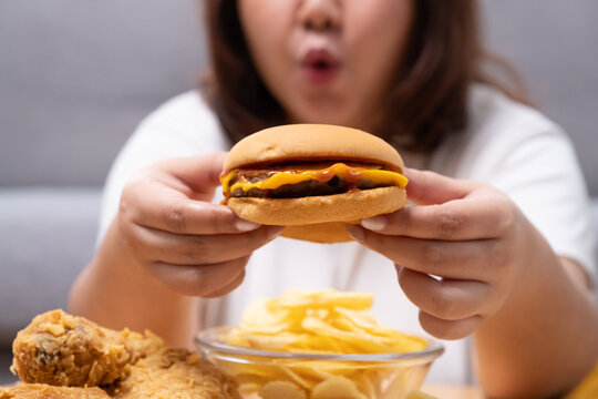 Young Asian oversize women gain weight while eating hamburger fried chicken, potato chips and French fried. Junk food that can cause obesity and unhealthy for human body.