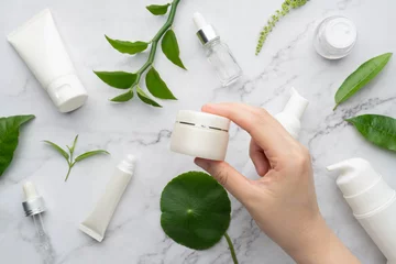 Poster Young female hand holding facial moisturizer cream bottle with organic natural skincare products on marble background. Beauty cosmetic skincare and cosmetology concept. © Orawan