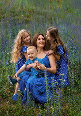 Happy smiling mom with three children in flowers in a park on a sunny summer day. Mother and children. Happy family.