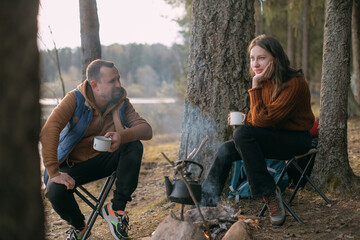 Family couple is resting on the shore of the lake with a tent. Fashing camp with a fire in the forest.