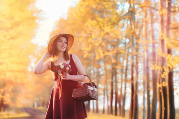 Fototapeta na wymiar A girl in a hat on a walk in the park. A girl with a basket walks in autumn. A girl is walking along the road at sunset.