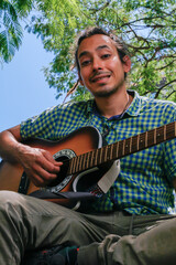 Young male, with dreadlocks hair, playing a brown acoustic guitar.