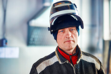 Male welder in work clothes with mask on his head looks directly into camera. Authentic portrait of...
