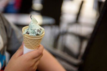 Menthol ice cream with chocolate chips close-up. A child's hand holds a delicious ice cream cone on the background of a summer cafe , snack, delicious food