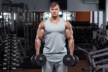 Muscular man working out in gym doing exercises with dumbbells, strong male