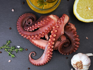 Cooked octopus tentacles on black slate plate served with spices, garlic, lemon and olive oil, top view of delicious sea food